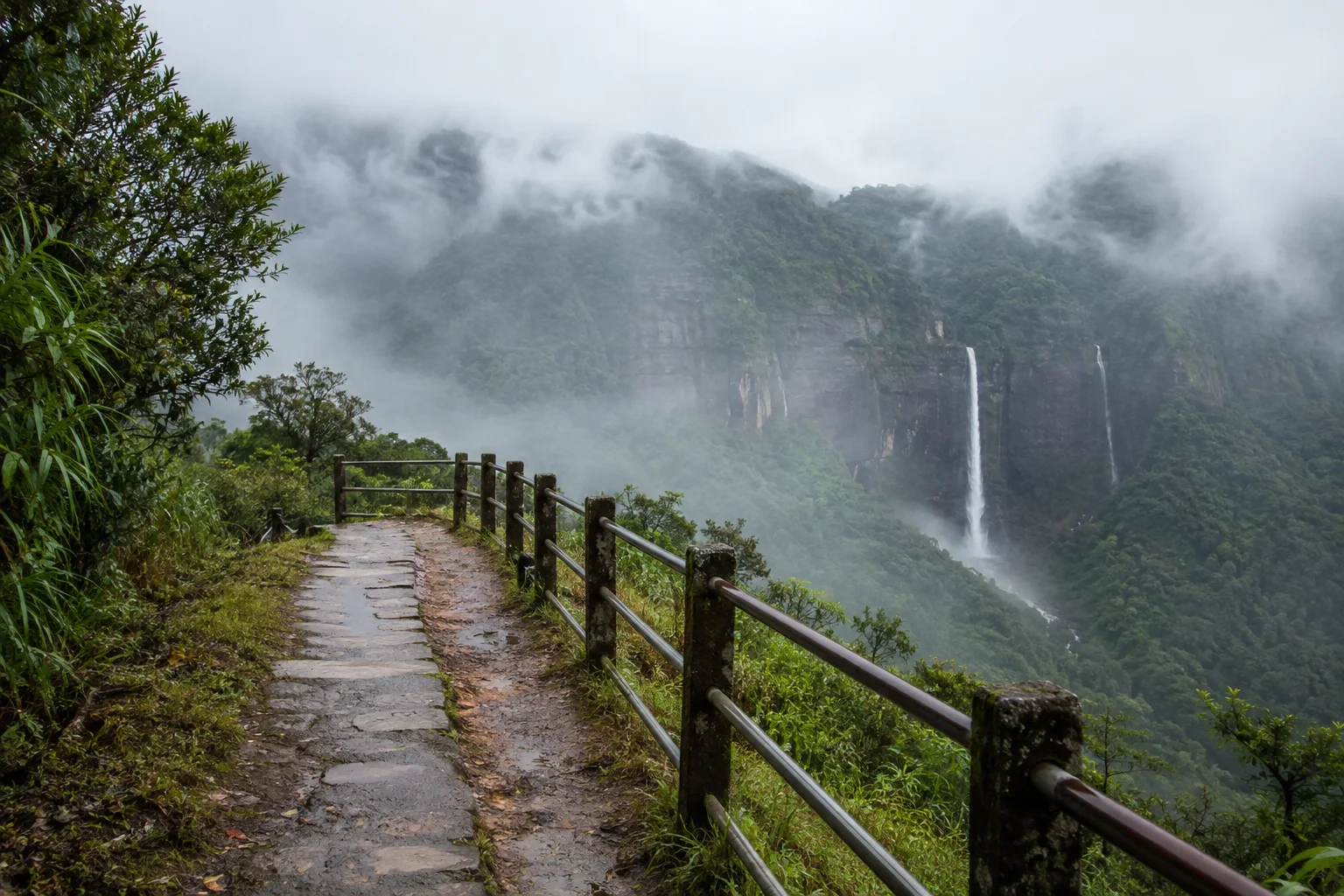 Влажная дорожка с ограждением у туманного ущелья в Khasi Hills